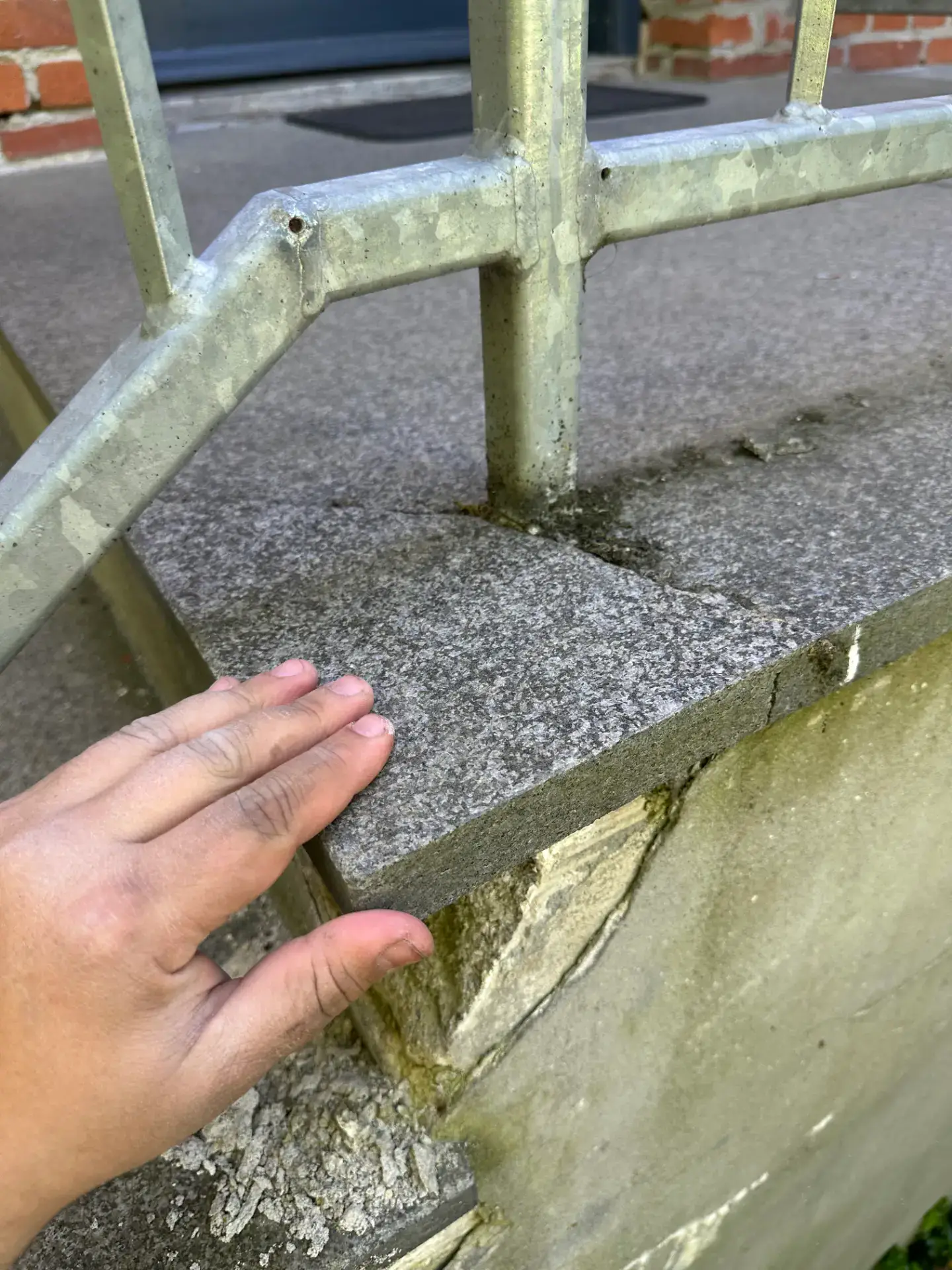 Støttemur med metalgelænder og stenbelægning.