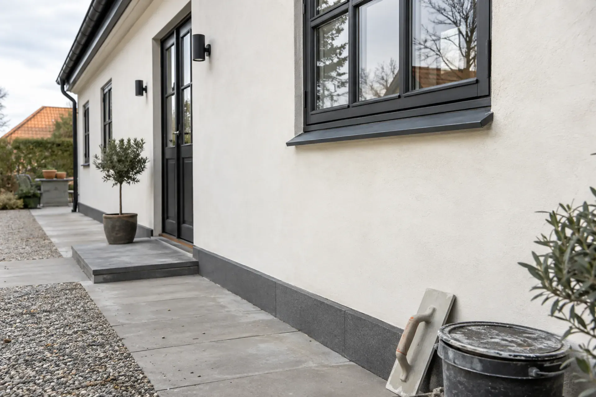 Facadepuds på hus med hvid facade og sort vinduesramme.